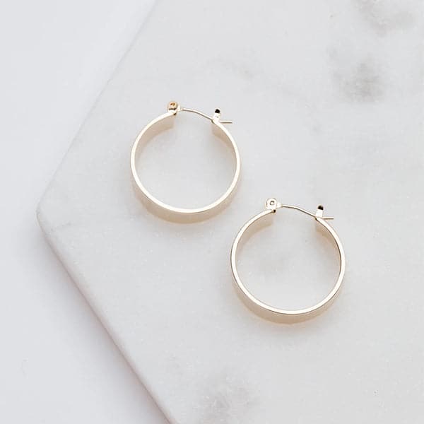 Medium sized silver hoops that have a wider frame and a thin depth. They feature a straight post and a clasp on the back top of the hoop to secure it on your ear.