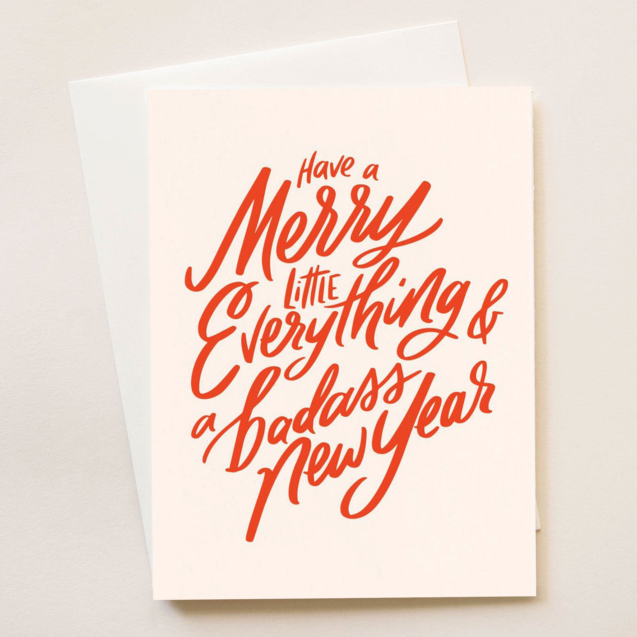 A light blush card with red writing that reads, "Have a Merry Little Everything & a badass New Year".