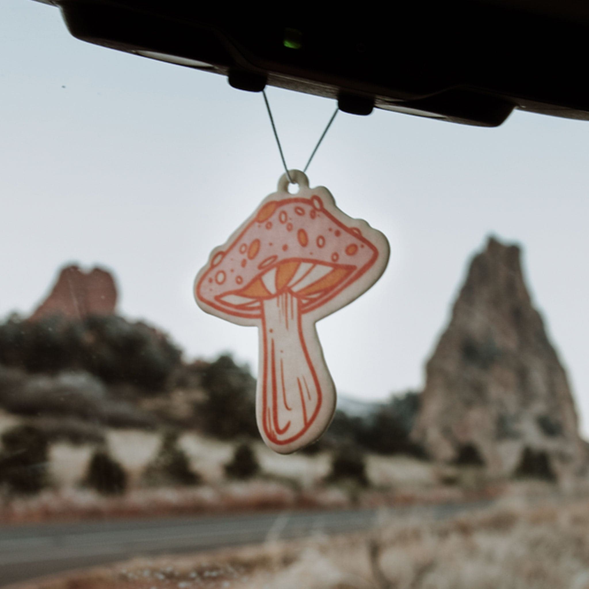 Mushroom air freshener with a soft pink cap and ivory stalk. The mushroom is bordered in red and has white and has orange and white spots. 