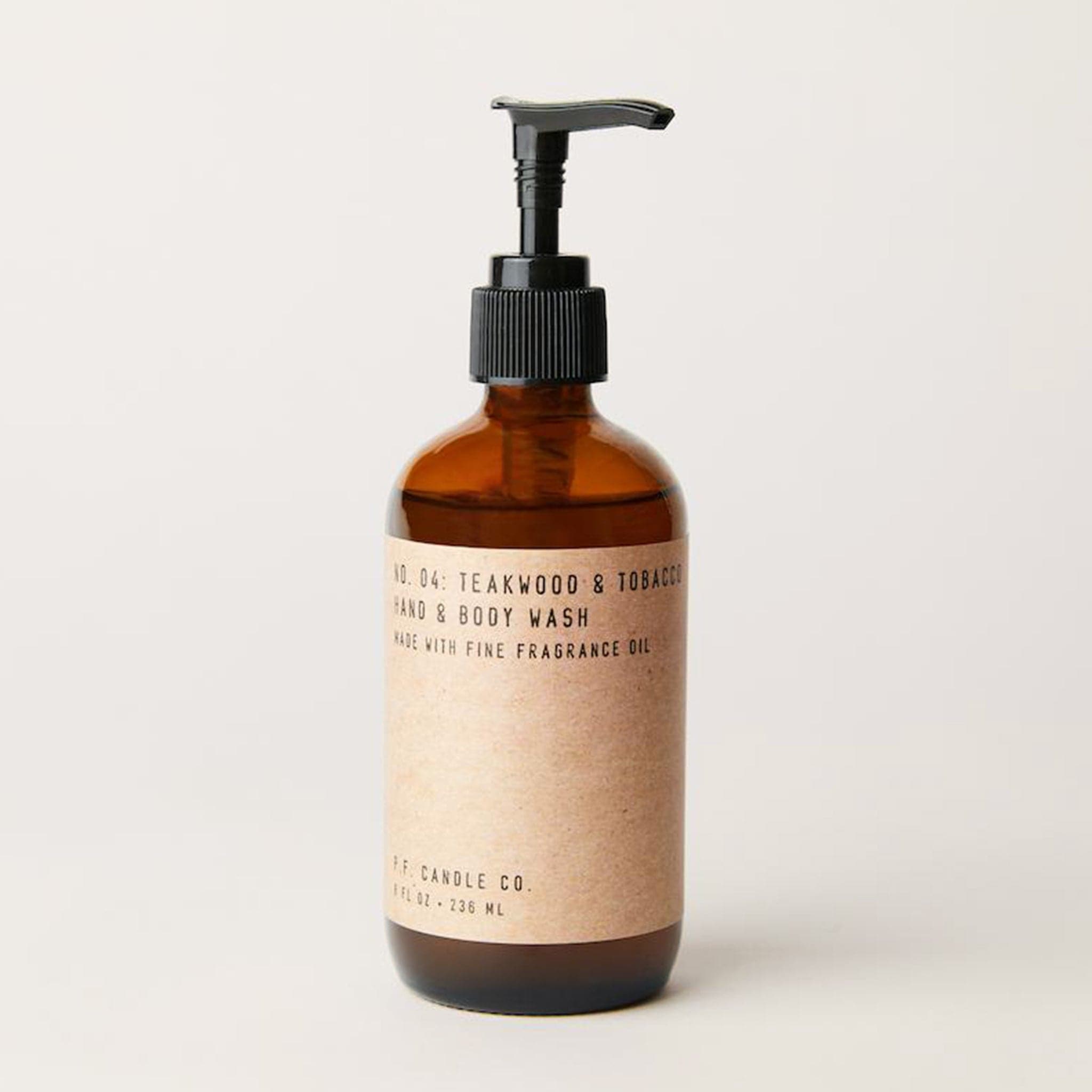 Against a white background is an amber brown, glass bottle with a black pump. On the front of the bottle is a brown wrap with black text. The black text reads ’Teakwood and Tobacco. Hand and body wash.’ 