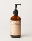 Against a white background is an amber brown, glass bottle with a black pump. On the front of the bottle is a brown wrap with black text. The black text reads ’Teakwood and Tobacco. Hand and body wash.’ 