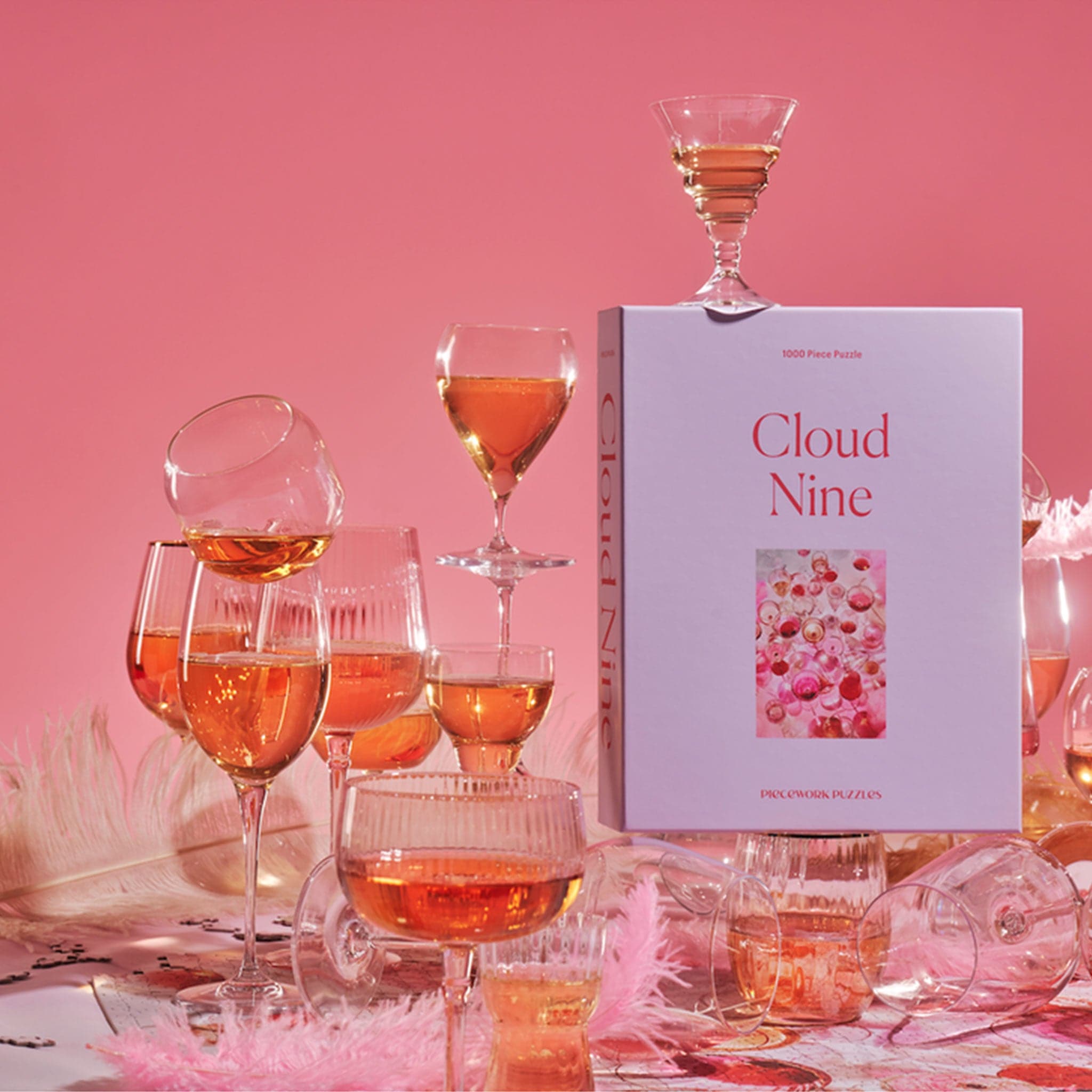 A lavender colored puzzle box that reads, "Cloud Nine" with a photo of what the puzzle looks like. The completed puzzle is a photo of an assortment of drinking glasses filled with a pink drink.