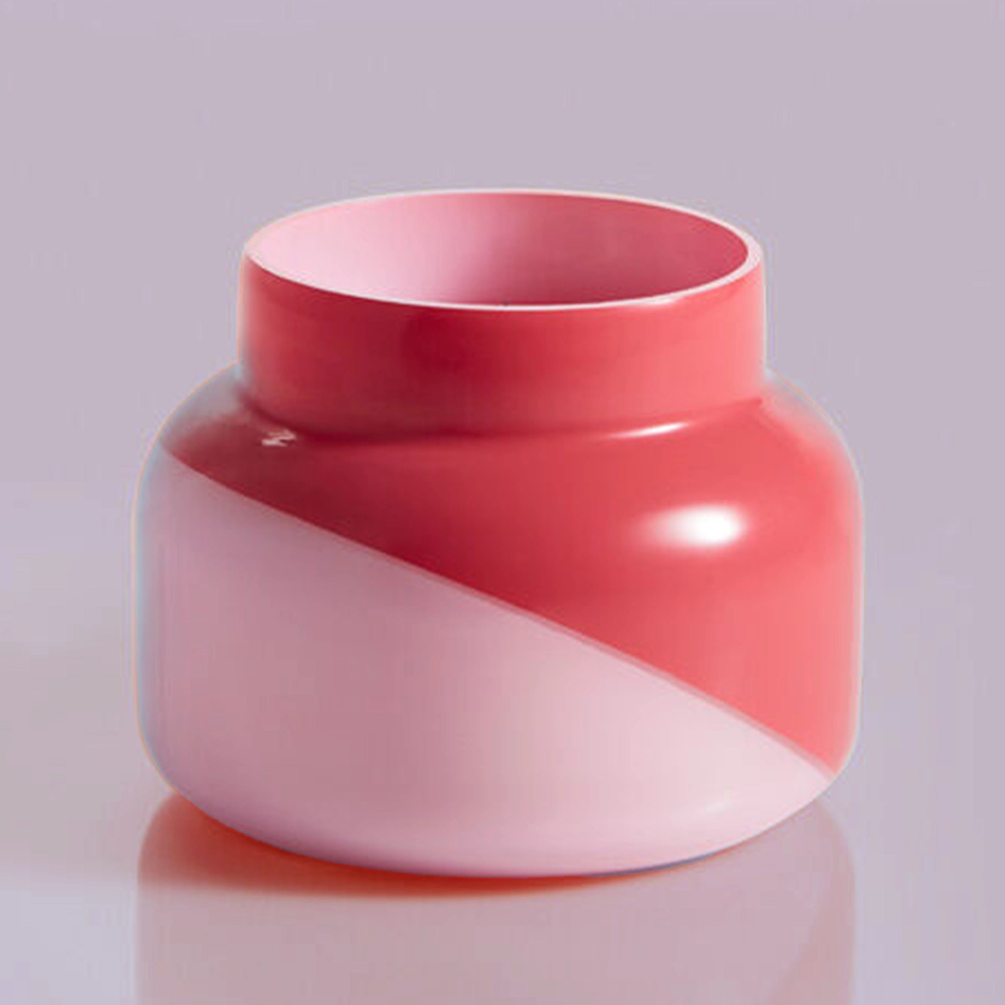 A glass candle jar with a two toned design featuring a light pink and a darker pink that is split diagonally.
