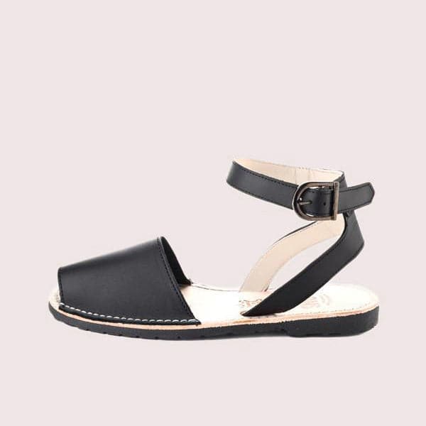 Single Avarca sandal made of lightweight dark rubber molded to a light natural leather sole. The sandal's front strap is dark black and large enough to cover the front half of foot. Above is a thin leather ankle strap of the same color with a dark buckle closure.