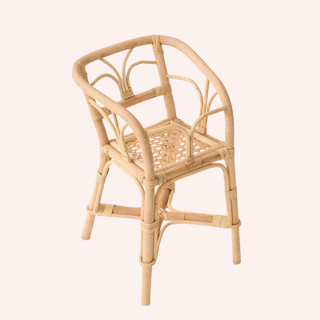 In front of a white background is a light tan wicker high chair. It has four legs. The chair has high arched sides and a back. The bottom of the seat is light tan cane.