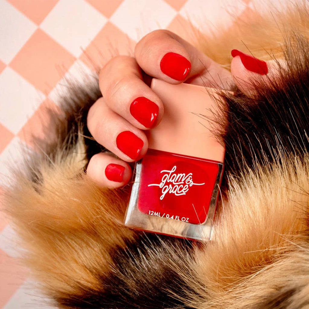 A bright red nail polish with a satin finish in a glass bottle with a peachy square lid.