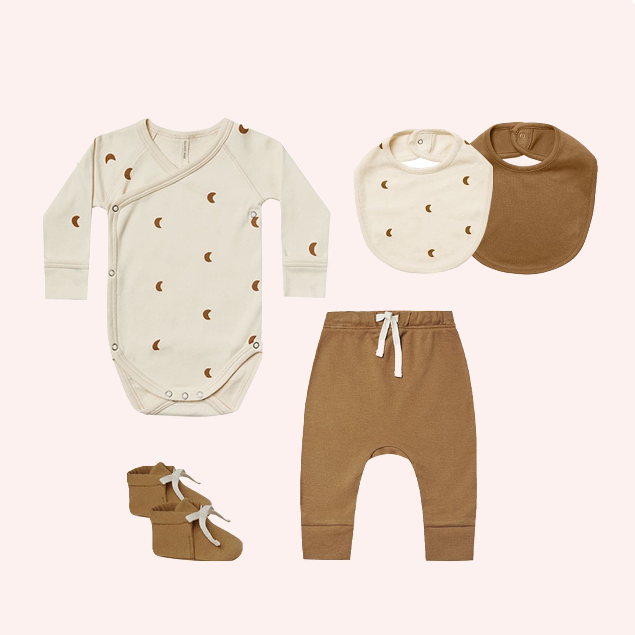 A five piece baby gift set. Ivory long sleeved onesie with brown crescent moon patterns. Ivory bib with brown crescent moon pattern. Brown bib. Brown joggers with white drawstring. Brown booties with white laces.