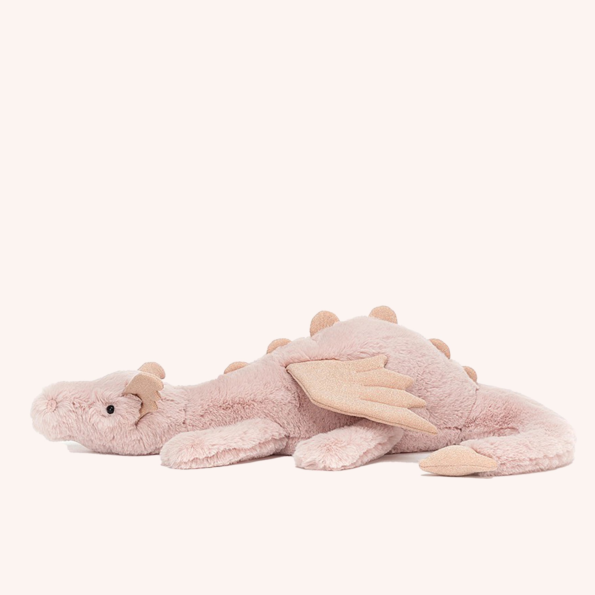 On a white background is a light pink dragon stuffed animal with wings, a sweet face and a long tail.