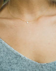 This is a picture of a close up of a model’s neck. The model has blonde hair and is wearing a gray sweater. Around her neck is a thin gold chain with a tiny gold heart in the middle.