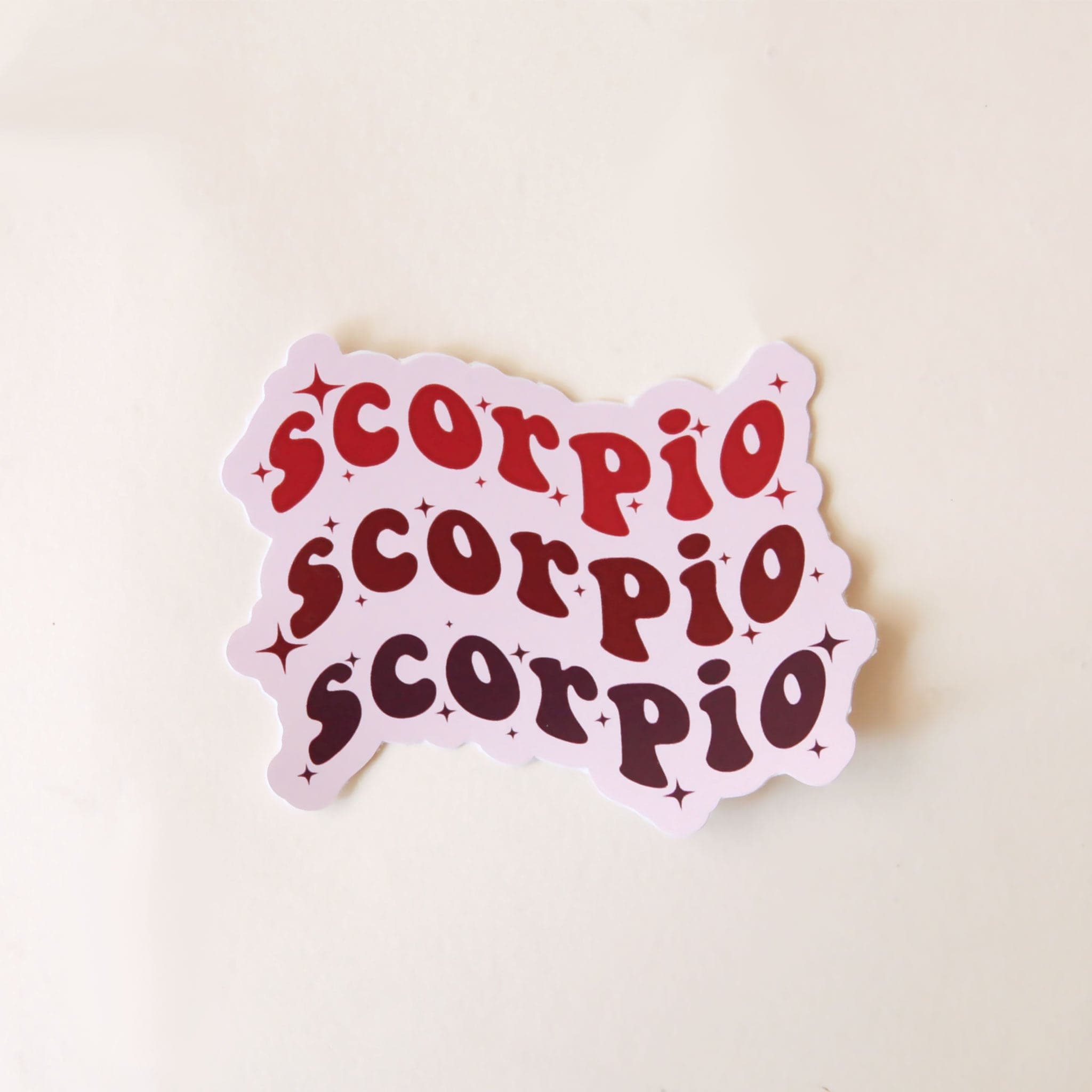 On a white background is a sticker with the word &quot;Scorpio&quot; stacked on top of one another three times in a wavy design. 