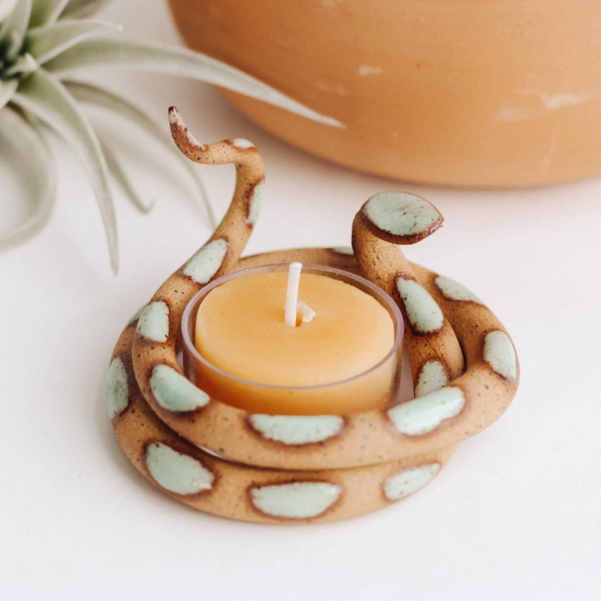 A tan ceramic tea light candle holder in the shape of a coiled up snake with turquoise spots. 