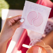 A model holding a pack of the eye gels that show a photo of two pink gel under eye masks with light purple text that reads, "Patchology, Serve Chilled Rosé Eye Gels".