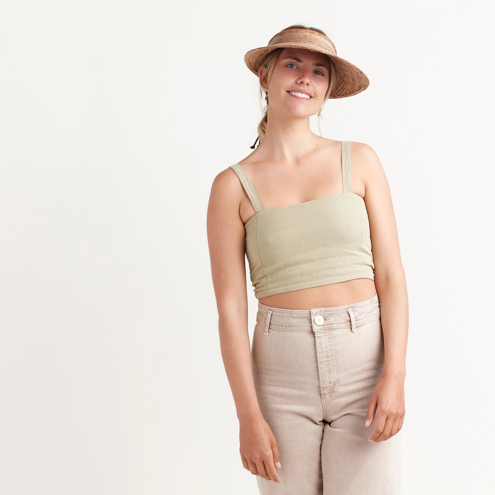 A woven straw visor hat with a large brim and beaded slip knot tie on the back that is adjustable, worn here on a model wearing a tank top and tan pants in front of a white background.