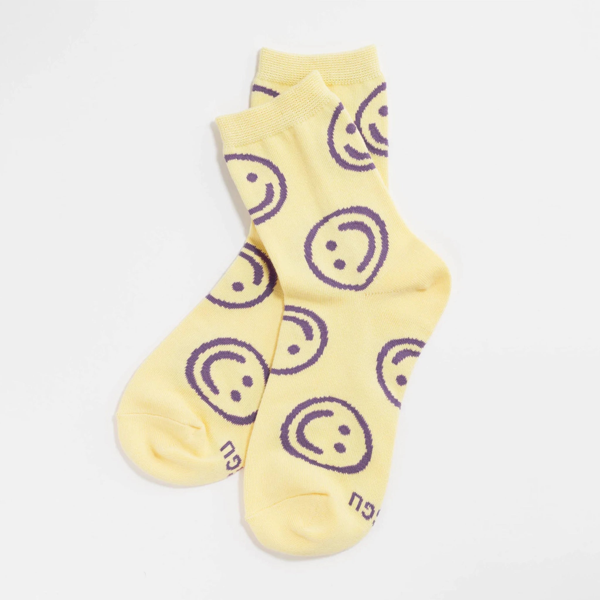 Light yellow crew socks with a repeating  purple smiley face design all over.