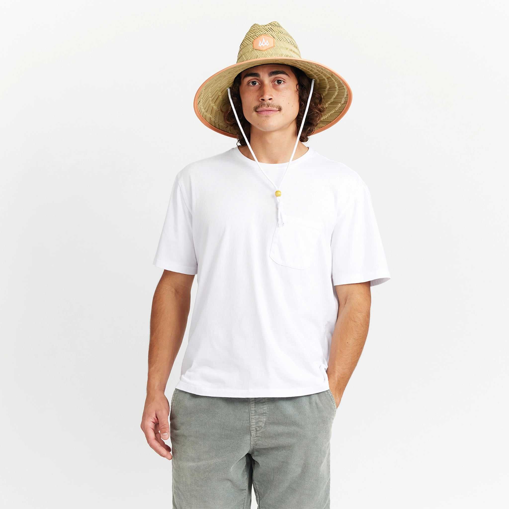 A wide brim sun set made of a neutral woven straw material with a white drawstring and tangerine orange detailing around the edge of the brim as well as the label in the center or the hat.