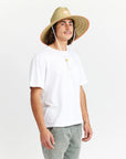 A wide brim sun set made of a neutral woven straw material with a white drawstring and tangerine orange detailing around the edge of the brim as well as the label in the center or the hat.