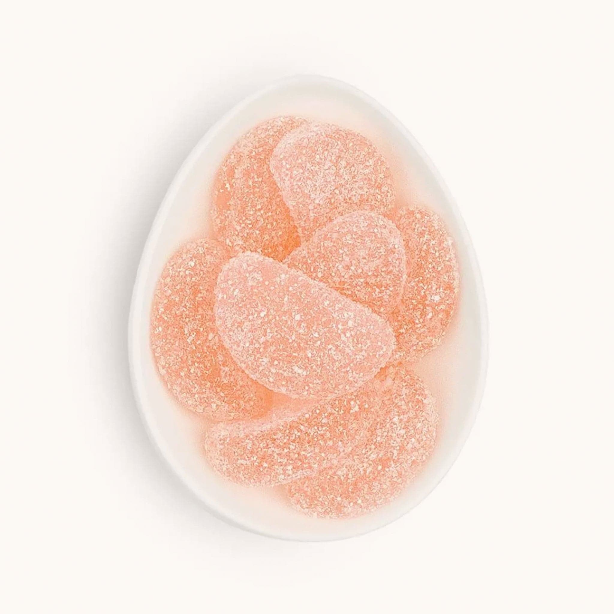 Half moon shaped grapefruit gummy slices covered in shimmering sugar crystals. The blush pink gummies are placed in a small white bowl. 