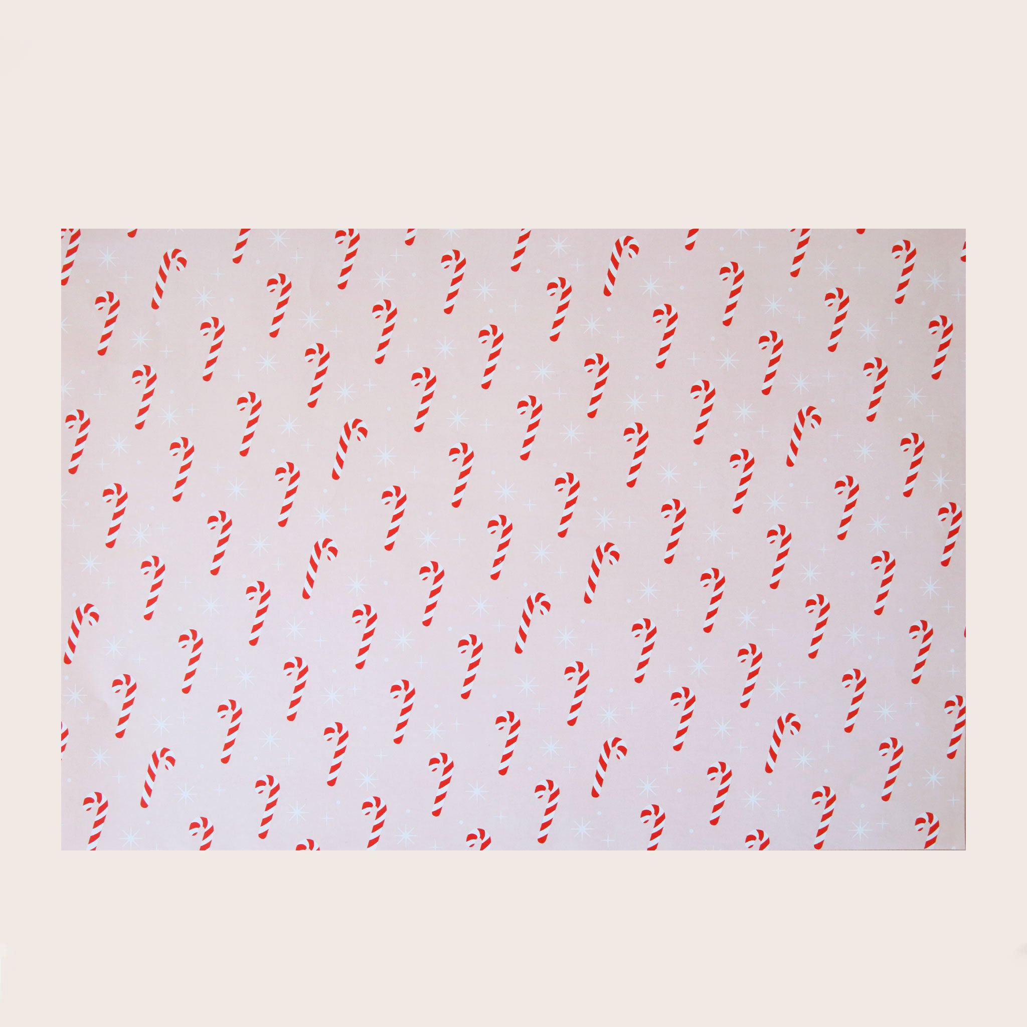 A single sheet of gift wrap with a blush background and a repeating red and white candy cane print. The gift wrap is reversible and the other side features a light purple / lavender background with an all over red and white candy cane design but the candy canes are slightly smaller than the reverse.