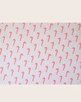 A single sheet of gift wrap with a blush background and a repeating red and white candy cane print. The gift wrap is reversible and the other side features a light purple / lavender background with an all over red and white candy cane design but the candy canes are slightly smaller than the reverse.