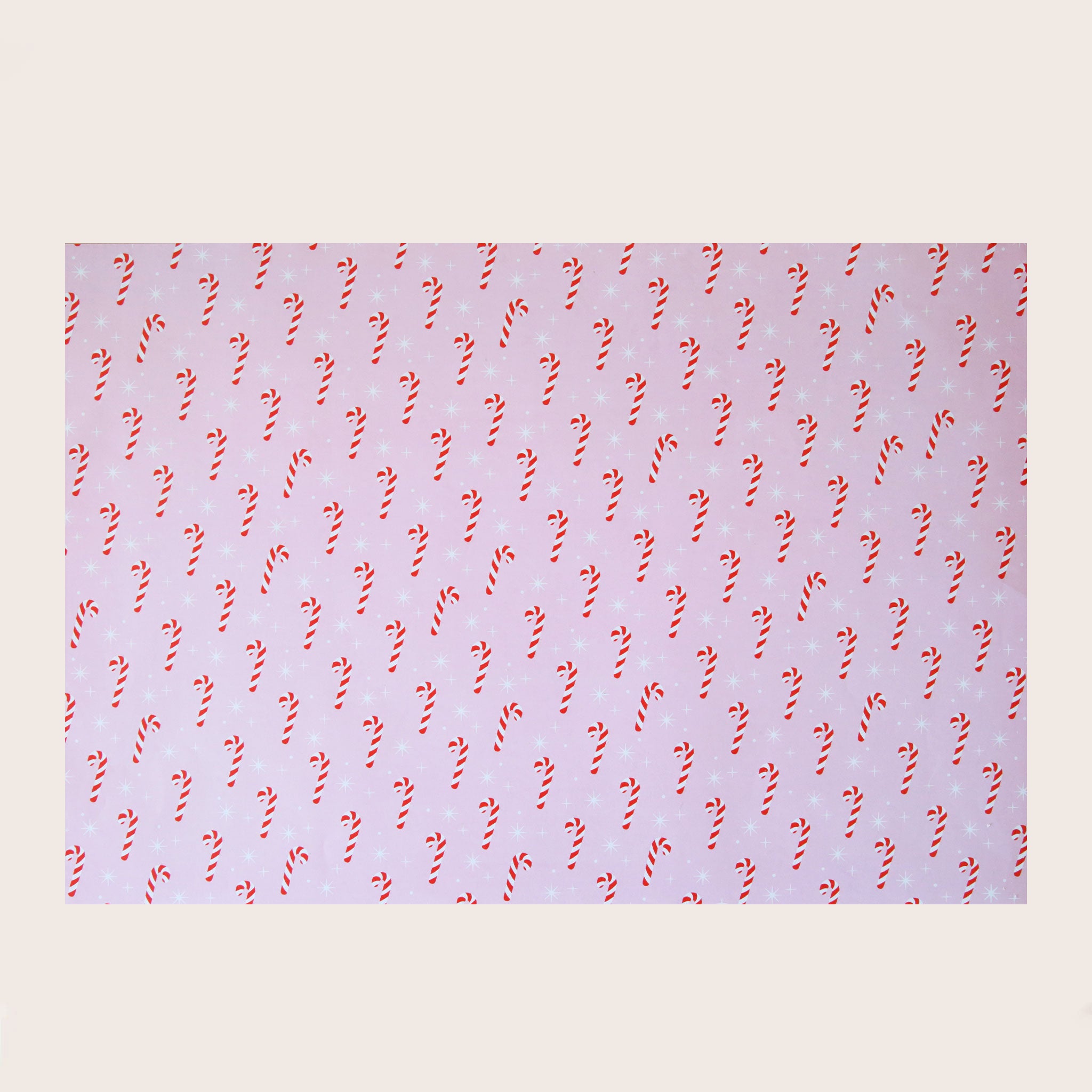 A single sheet of gift wrap with a blush background and a repeating red and white candy cane print. The gift wrap is reversible and the other side features a light purple / lavender background with an all over red and white candy cane design but the candy canes are slightly smaller than the reverse.