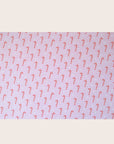 A single sheet of gift wrap with a blush background and a repeating red and white candy cane print. The gift wrap is reversible and the other side features a light purple / lavender background with an all over red and white candy cane design but the candy canes are slightly smaller than the reverse.