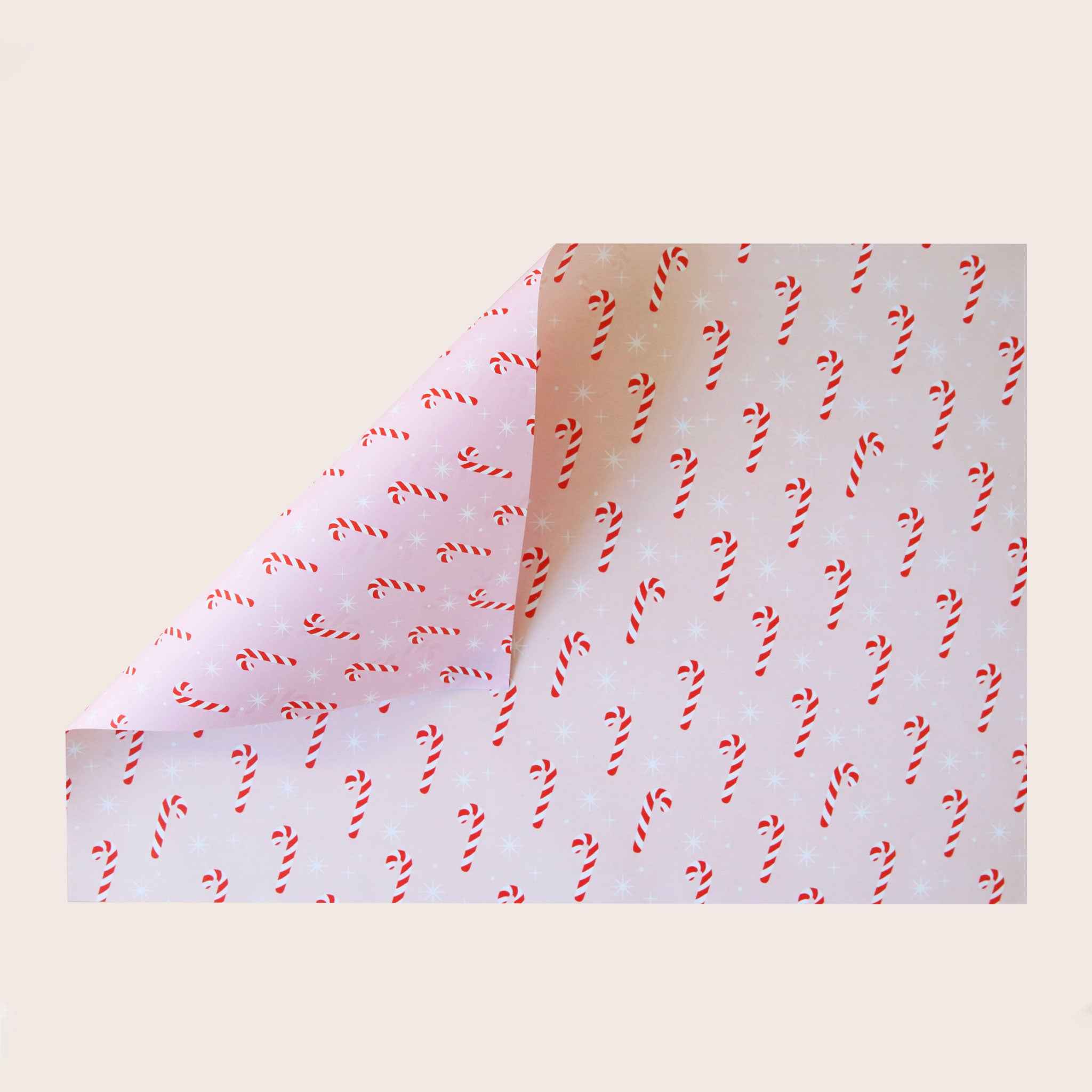 A single sheet of gift wrap with a blush background and a repeating red and white candy cane print. The gift wrap is reversible and the other side features a light purple / lavender background with an all over red and white candy cane design but the candy canes are slightly smaller than the reverse.