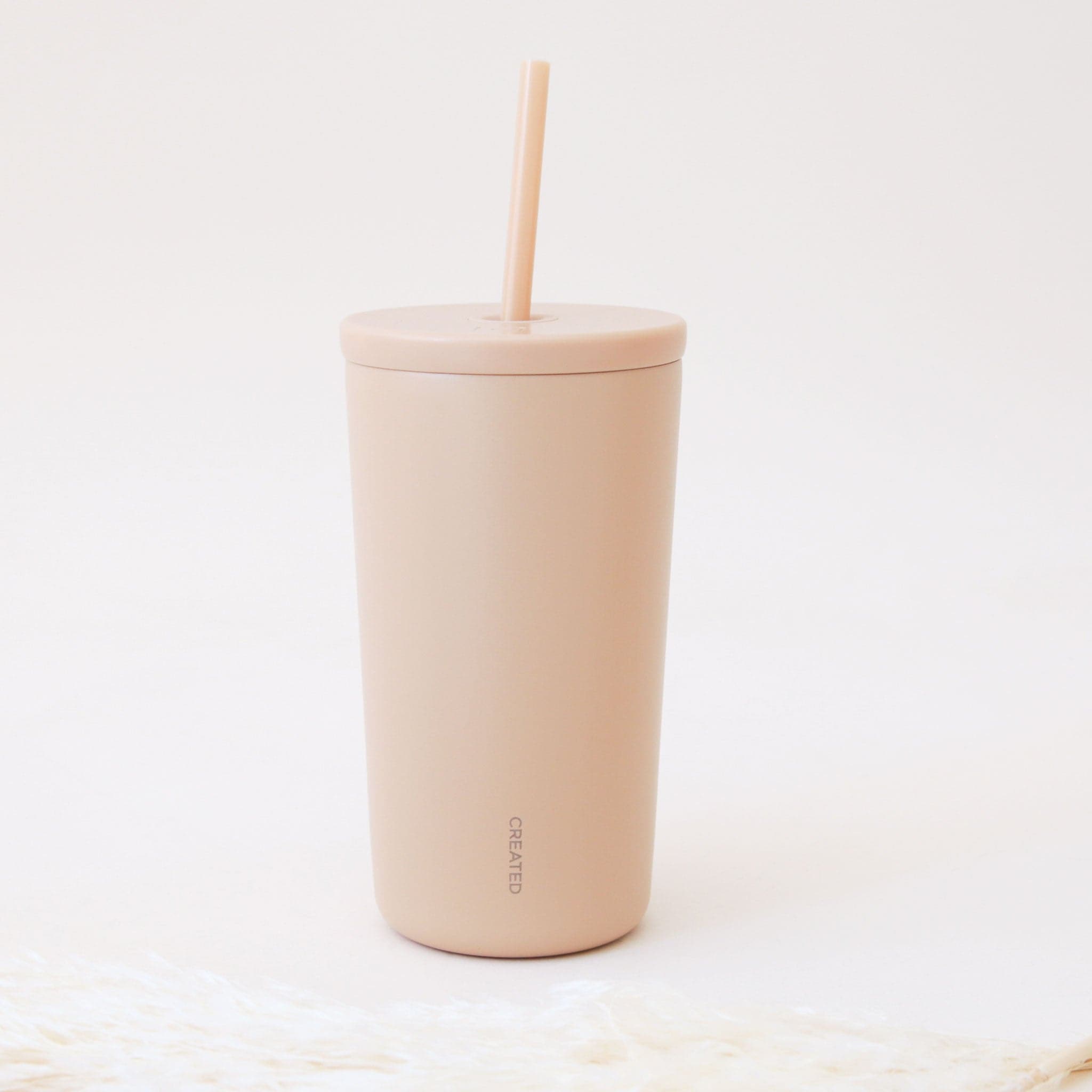 A lighter pink iced travel cup with a straw and small text that says, "Created".