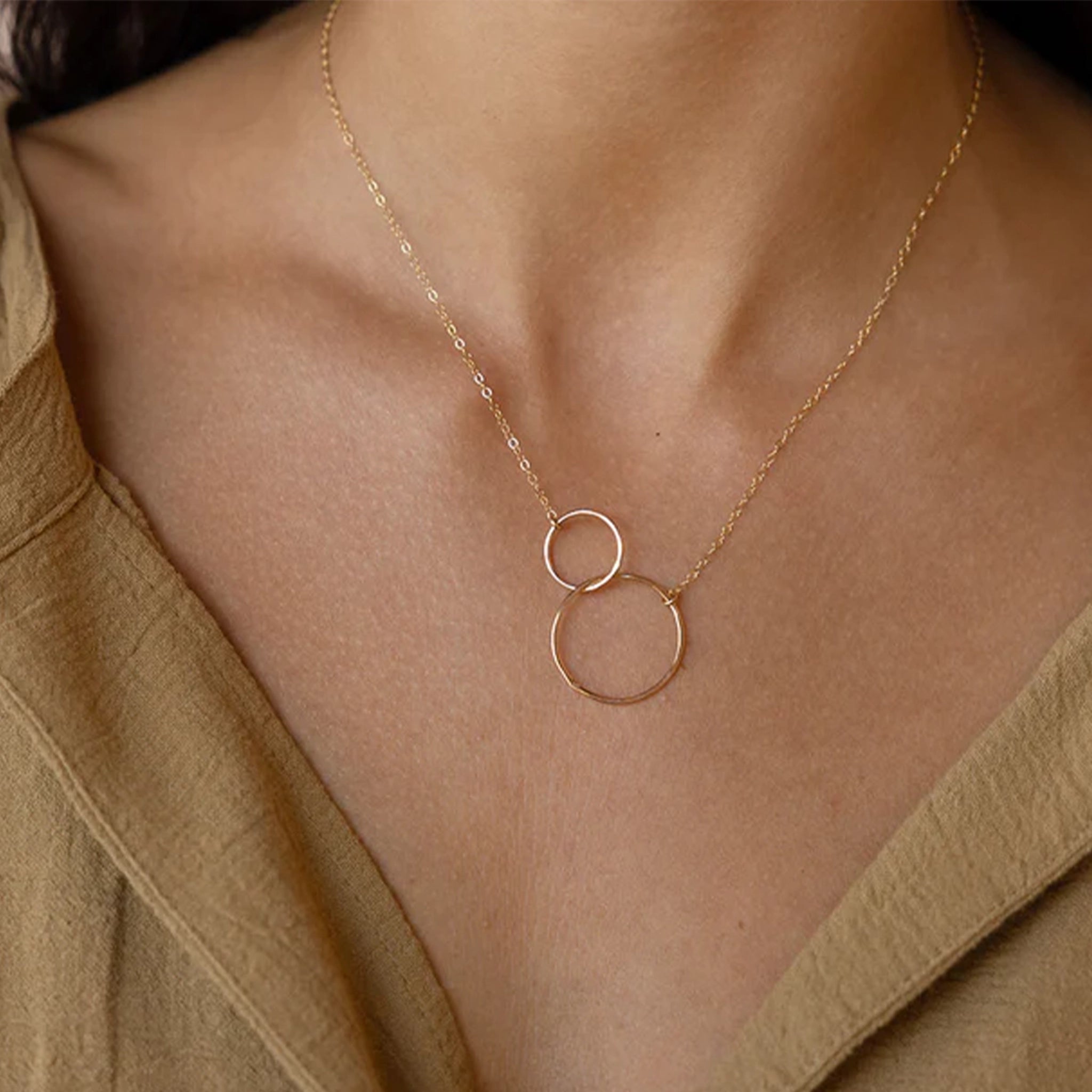 A model wearing the unity necklace features two gold circles, hand forged and lightly hammered that come together and hang from a beautiful chain.