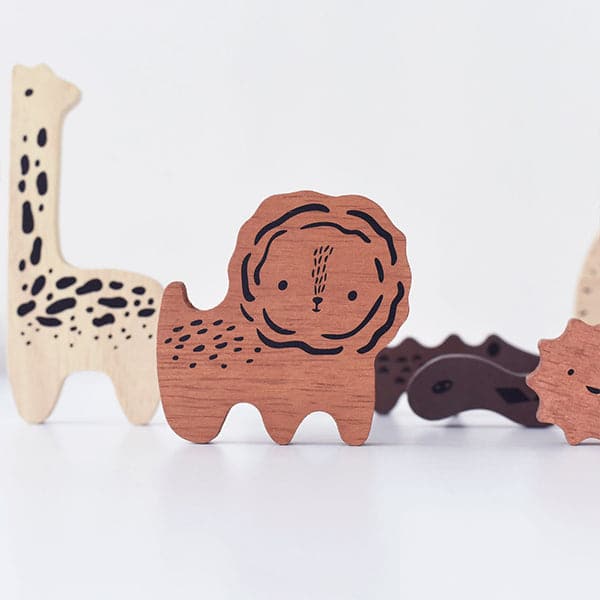 Wooden puzzle pieces shaped as animals including a beech wood giraffe, teak colored lion and chocolate snake. Each piece is displayed standing upright as if the animals were standing themselves. The animals lay against a solid white background.