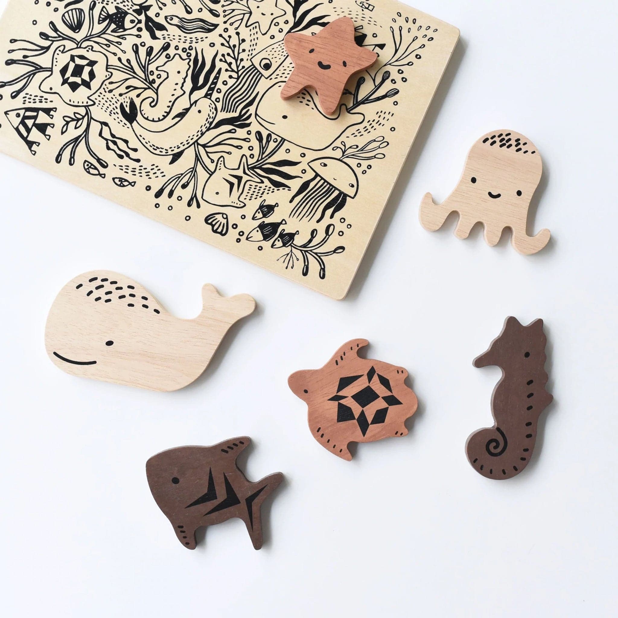 Sweet sea creatures scattered around their puzzle board. There is a starfish, octopus, sea horse, turtle, fish, and whale. Each puzzle piece is wooden and a different color wood. On the back on the puzzle is an adorable sea illustration with a plethora of sea wildlife.