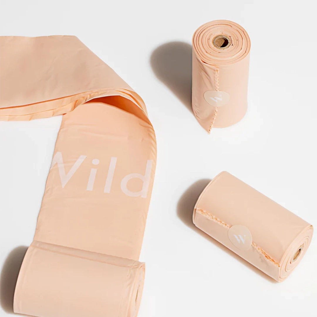 A photograph of the poop bags outside of the packaging. They are a salmon color and have white text on each bag that reads, "WILD".