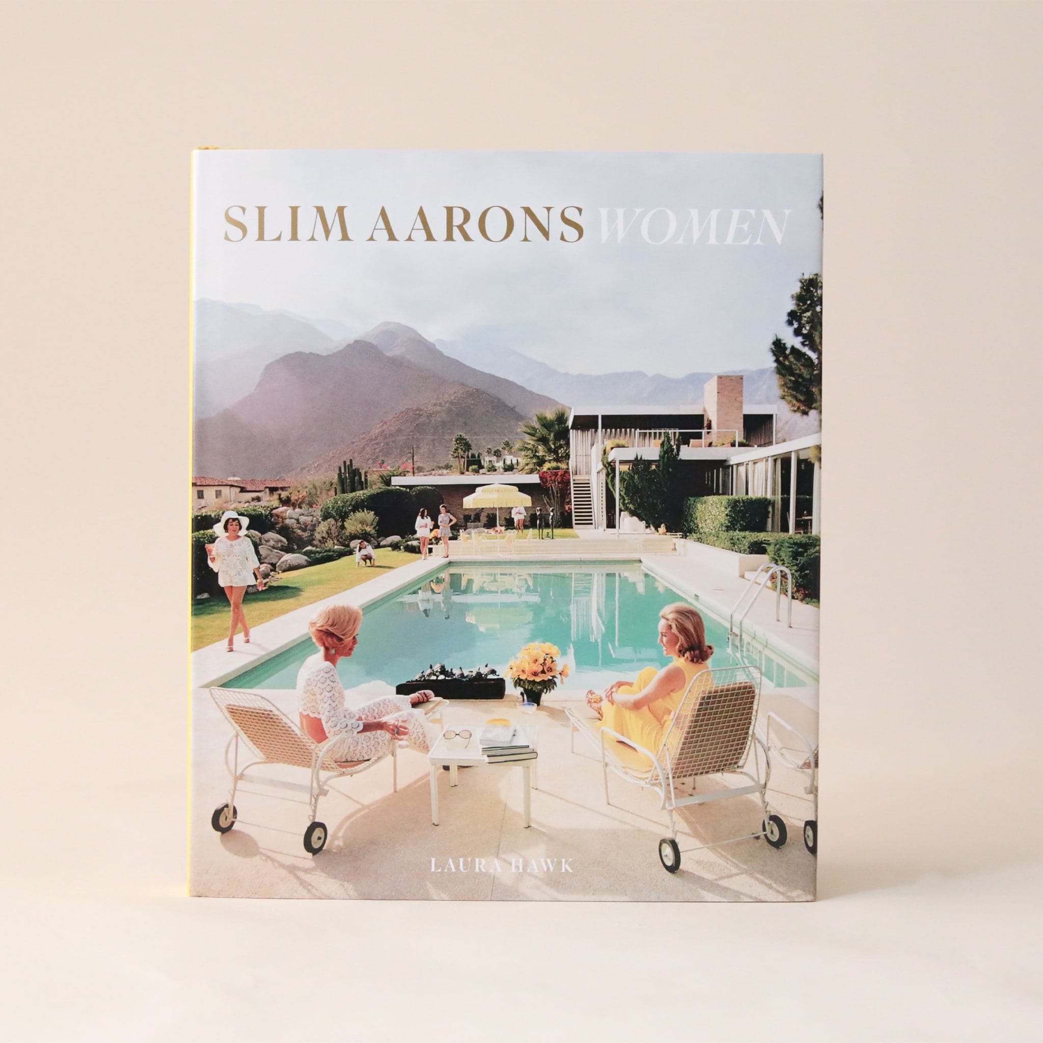 A book cover featuring a photo of 3 women around a pool outside of a midcentury home with a beautiful mountainous background. The title reads, &quot; Slim Aarons Women&quot;.